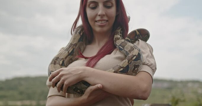 A happy, young woman smiles as she holds her pet snake around her shoulders.