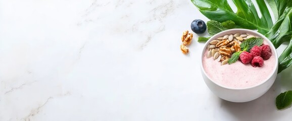 Healthy pink smoothie bowl with berries nuts seeds mint and tropical leaf on marble surface fresh food
