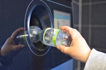 A woman hands over plastic bottles to a recycling machine.