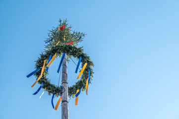 Maibaum mit Nadelbaum und Kranz und wehenden Bändern im Gegenlicht vor blauem Himmel in Neckartenzlingen