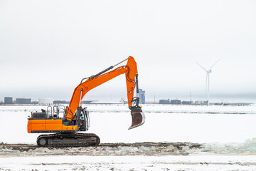 A powerful heavy orange tracked excavator digs ice on a clear winter day.