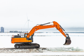 A powerful heavy orange tracked excavator digs ice on a clear winter day.