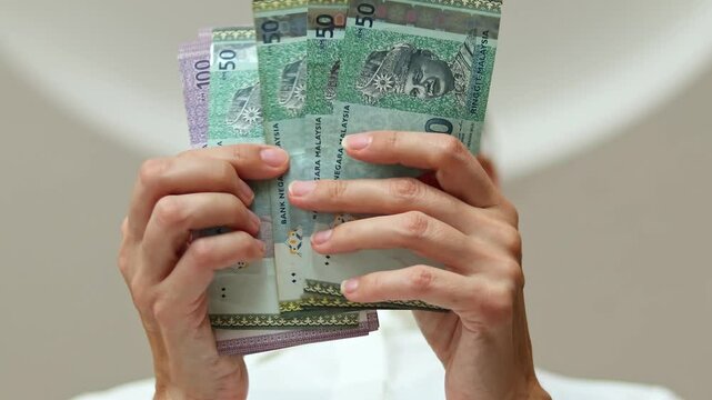 Closeup shot of woman's hands and Malaysian ringgit (MYR) banknotes. Concept of office work, saving money for retirement, cash settlement, financial success, literacy and income planning in Malaysia.