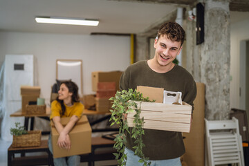 young man carrying a crate with stuff and plant for his new apartment