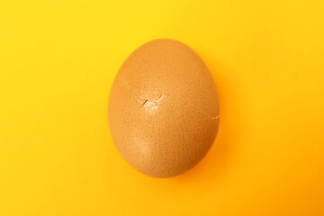 One egg with cracked shell on orange background, top view