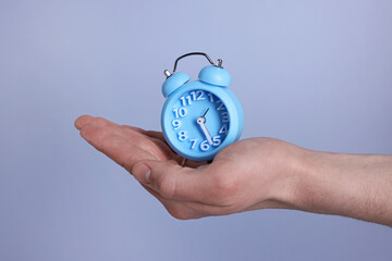 Man with light blue alarm clock on grey background, closeup