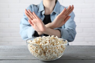 Woman refusing to eat popcorn at grey wooden table, selective focus. Food allergy concept