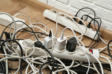 Extension power boards overloaded with plugs on wooden floor, closeup