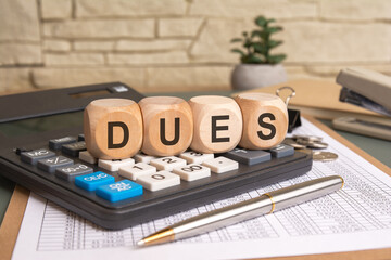 Dues text on wooden blocks with calculator and financial documents in office background.
