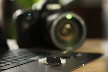 SD memory cards, holder, laptop and photo camera on wooden table, closeup