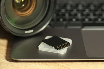 SD memory card, holder, photo camera and laptop on wooden table, closeup