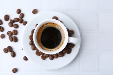 Aromatic coffee in cup and beans on white tiled table, flat lay. Space for text
