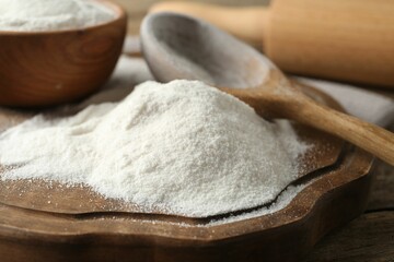 Wheat flour and spoon on wooden table, closeup