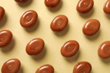 Many tasty caramel candies on beige background, flat lay