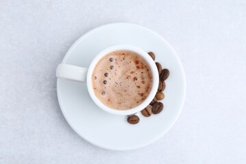 Aromatic coffee in cup, beans and saucer on light table, top view