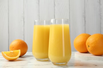 Orange juice in glasses and fresh fruits on white marble table, closeup