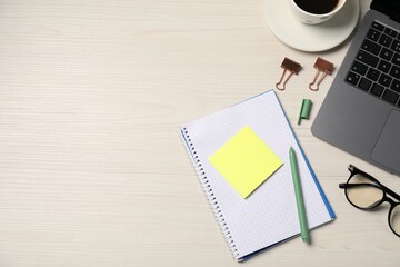 Notebook, sticky note, pen, glasses, binder clips and laptop on wooden table, flat lay. Space for...