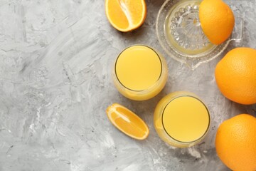 Orange juice in glasses, fresh fruits and juicer on grey table, flat lay. Space for text