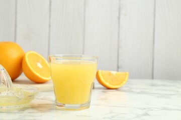 Fresh orange juice, fruits and squeezer on white marble table against wooden background, closeup. Space for text