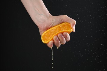 Woman squeezing orange on black background, closeup