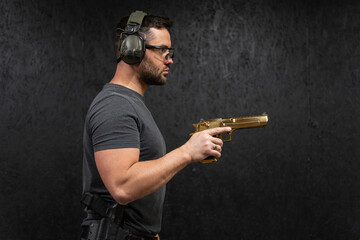 Man wearing protective glasses and ear protection holds a luxurious golden pistol, ready for accurate shooting indoors.