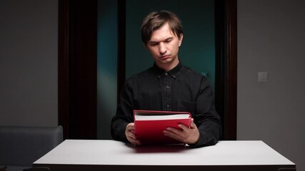Man holding red book over white table in dark room