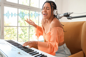Young African-American woman with microphone and synthesizer singing in studio