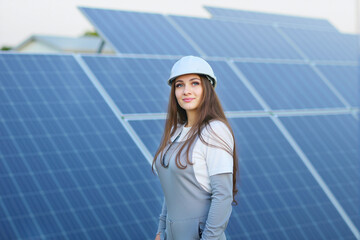 Friendly Female Technician in Hard Hat and Overalls Looking at Camera at Solar Farm, Portrait View.