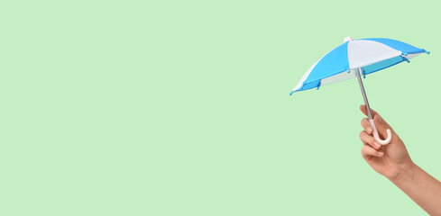 Female hand with mini umbrella on green background