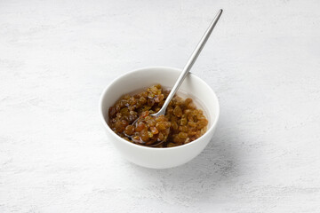 Soaked golden raisins in a white bowl with water and spoon on light background, healthy ingredient