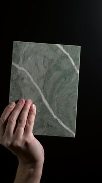 Luxury quartz stone texture pattern with trendy curly veins. Marble slab in hand on black background in Slow motion