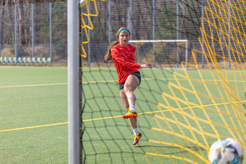 Obraz premium Sporty girl scores a goal into the goal. Football concept. Girl on the football field.