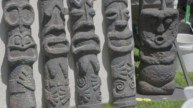 This video shows a panning of tropical carved stone tiki figurines on a sunny day.