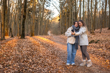 Fototapeta premium Two friends taking a selfie on their phone in the forest. Friends in nature.