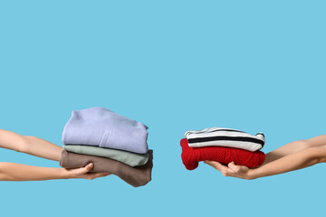 Many female hands with stacks of different clothes on blue background