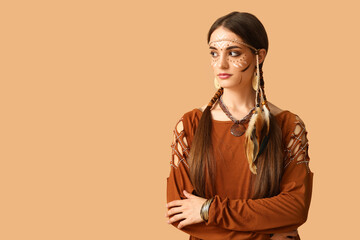 Beautiful young woman in Indian costume on beige background. Native American Heritage Month