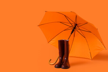 Stylish umbrella and gumboots on orange background