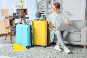 Male tourist with laptop and suitcases booking hotel room online at home