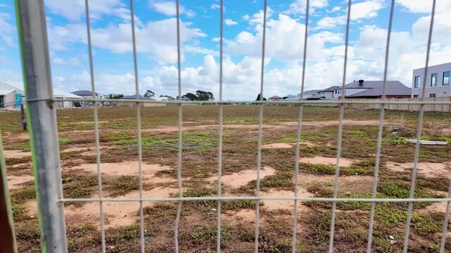 View through temporary construction fencing of an empty residential lot in Werribee, Melbourne's growing outer suburb, cleared and vacant land surrounded by newly constructed modern homes in Australia