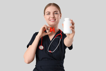 Female endocrinologist with thyroid gland model and pill bottle on grey background