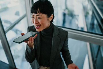 Businesswoman recording voice message on smartphone in modern office