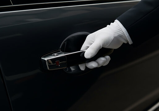 A hand in a white glove opens a sleek, black car door with a focus on service and elegance.