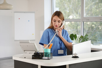 Female medical intern talking by telephone at reception in clinic