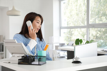 Female Asian medical intern talking by telephone at reception in clinic