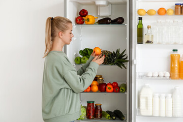 Young woman choosing food in modern fridge at home