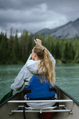 Fototapeta premium Young woman sitting in a canoe or kayak in a mountainous location on vacation, relaxing vacation concept 