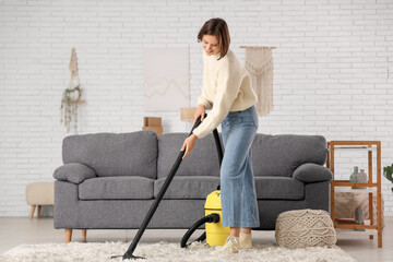 Beautiful young woman cleaning carpet with modern vacuum cleaner at home