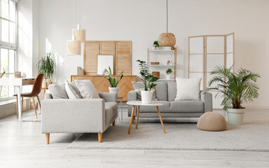 Interior of living room with grey sofas, folding screens and plants