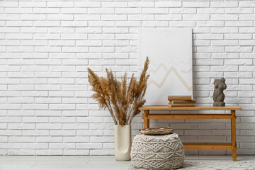 Bench with old books, picture and statuette near white brick wall in interior of room