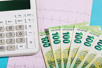 Cash euros and calculator on electrocardiogram. Calculating the cost of health insurance
